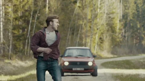 Scared man running in slow motion from the chasing car through the forest road Stock Footage 82740064