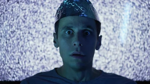 Scared man wearing tin foil hat in a front of TV screen Stock Footage 165595696