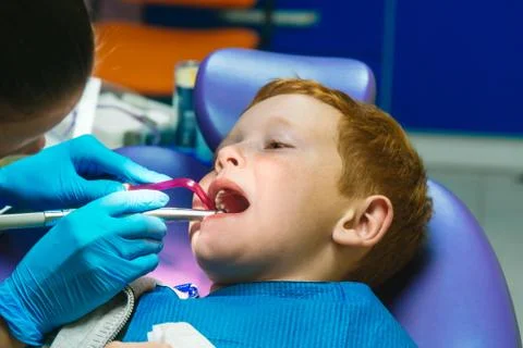 Scared red-haired boy crying at reception at dentist in dental chair Stock Photos