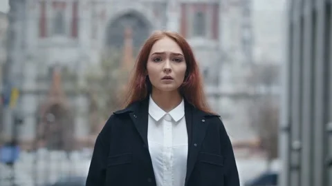 Scared red-haired girl looking at camera on the city background. Worried young Stock Footage 238931520
