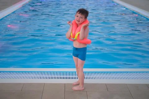 Scared sad boy with floating vest standing at edge of swimming pool. Child af Foto stock