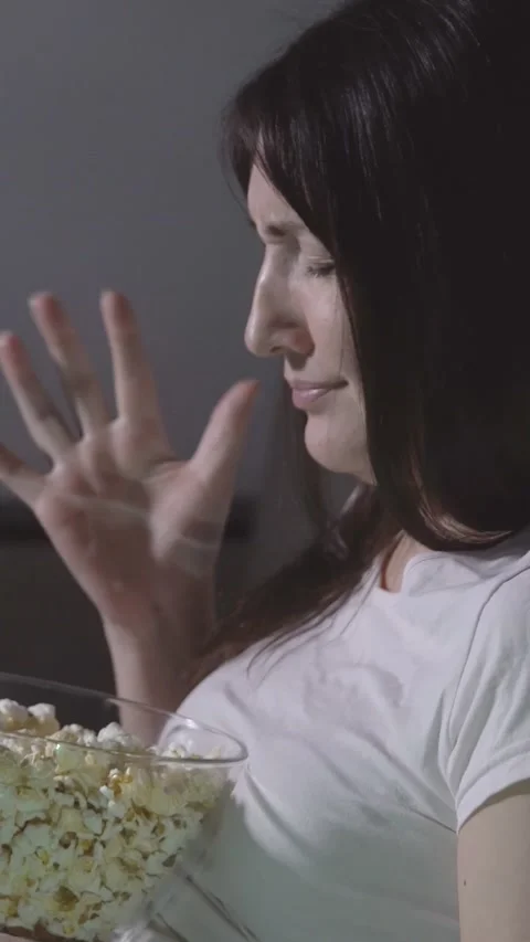 Scared woman eating popcorn while watching a horror movie at night, showing Stock Footage 345406545