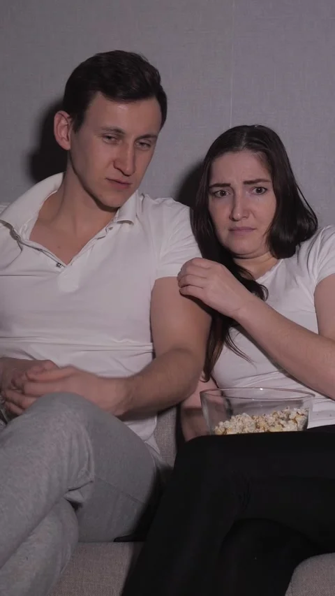 Scared young couple watching a horror movie together, eating popcorn at home on Stock Footage 341678305