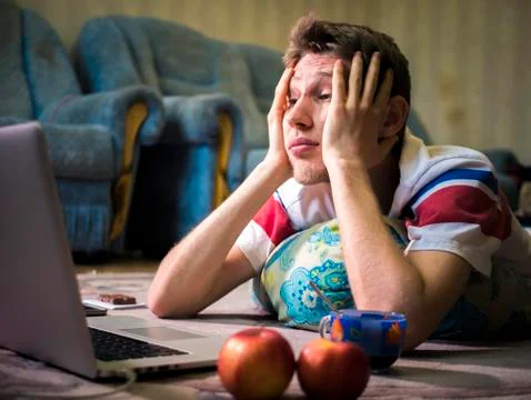 Scared young man lying on the floor and watching horror film Stock Photos