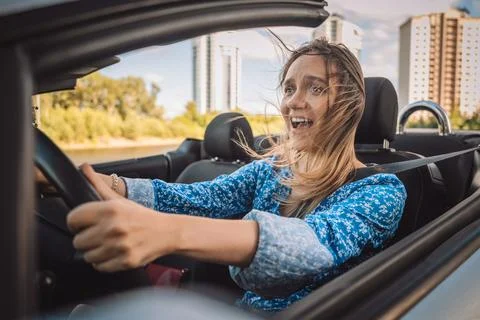 Scared young woman screaming while driving a convertible car. Driving phobi.. Stock Photos