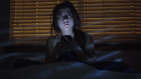A scared young woman using smartphone on bed - Reenactment Stock Footage 202912255
