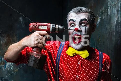 The scary clown and electric drill on dack background. Halloween concept Stock Photos