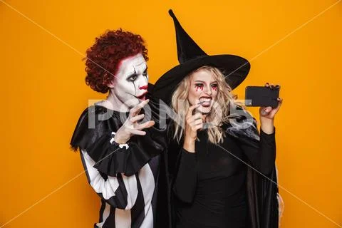 Scary clown and witch making selfie on smartphone isolated Stock Photos