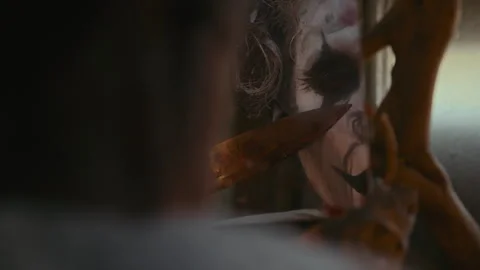 Scary Clown Looking at Himself at Mirror and Dragging Knife across His Face Stock Footage 250946954