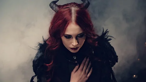 Scary demon doing witchcraft. Red-haired girl witch with black horns sitting on Stock Footage 137193101