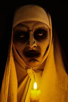 Scary devilish possessed nun standing with a candle in a dark room. Horrors a Stock Photos