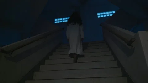 Scary halloween ghost ascends dark stairs, wears white costume, long black hair, Vídeos de archivo 343827080