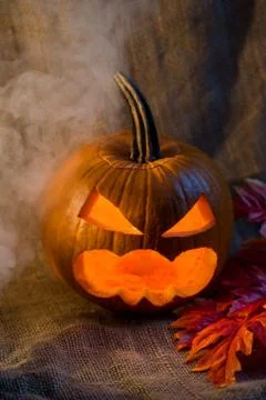 Scary jack-o-lantern, light inside and red leaves Foto stock