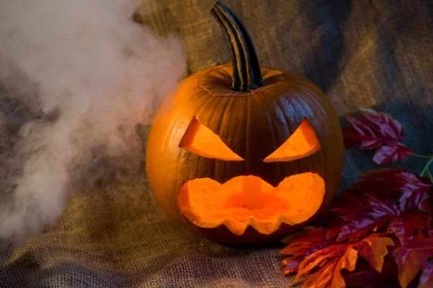Scary jack-o-lantern, light inside and red leaves Stock Photos