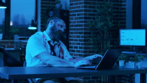 Scary looking zombie trying to work on modern laptop in office workspace at Stock Footage 197720809