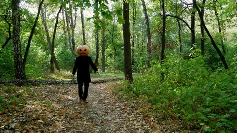 Scary pumpkin-headed man chasing after someone in the forest. Knife in hands.  Stock Footage 116489365