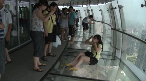 Scary shot. Girls sits on glass floor of tower - pan down Stock Footage
