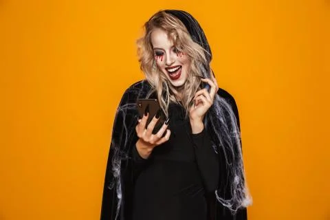 Scary wizard woman wearing black costume and halloween makeup holding smartph Stock Photos