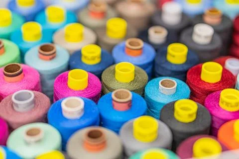 A scatter of multi-colored thread spools on a neutral background, arranged in Stock Photos