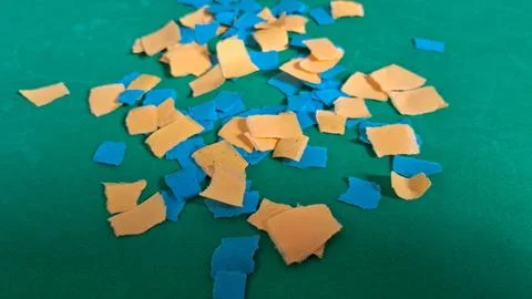 Scattered blue and orange paper pieces on a vibrant green surface Stock Photos