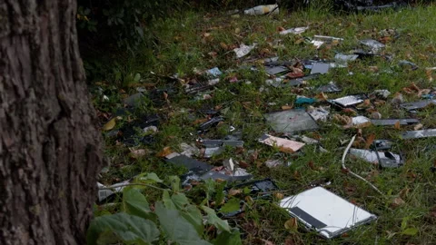 Scattered electronic waste and broken devices cover grassy ground beside rough Stock Footage 344968392