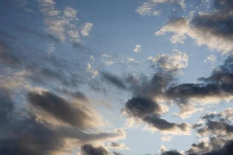 Scattered evening clouds illuminated by warm sunlight over clear blue sky Fotos Stock