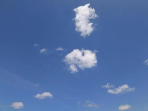 Scattered fluffy white clouds floating across a bright blue sky on a clear day Stock Photos
