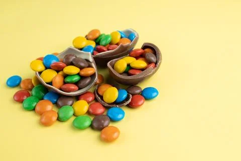 Scattered multi-colored candies in broken Chocolate Easter eggs on yellow Stock Photos