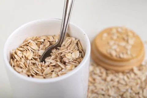 Scattered oat flakes in a ceramic container with a metal spoon. Healthy food  Stock Photos