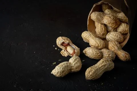 Scattered peanuts from a paper envelope on a black background. Stock Photos