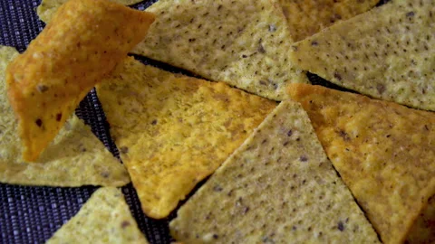Scattered triangular corn nacho chips with spices rotating on dark textured mat Stock Footage 345610904