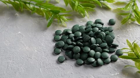 A scattering of Chlorella spirulina tablets on a gray background with algae Stock Photos