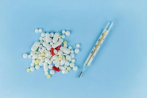 A scattering of different pills on a blue background and a thermometer with.. Stock Photos