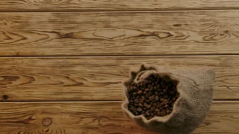 Scattering roasted coffee beans from falling traditional burlap bag . Top view Stock Footage 138521680