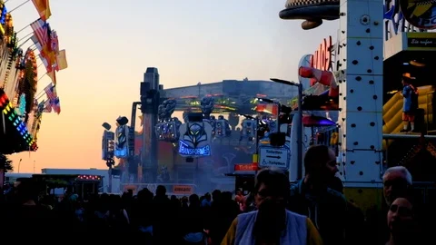 Scene with crowd of people and thrill rides at a funfair during dusk or sundawn Stock Footage 95919113
