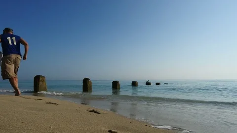 Scene of dock pilings on beach man jogs by Stock Footage 72580672