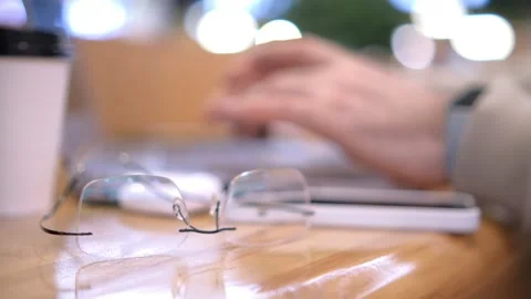 A scene with glasses on a table and hands typing on a laptop in the blurred Stock Footage 276536260
