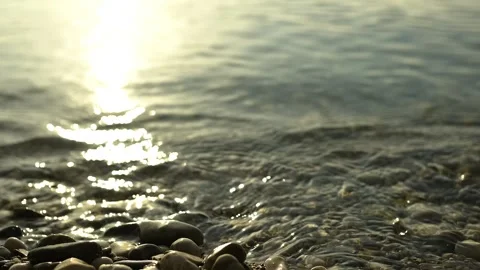 Scene of a lakeshore with pebbles in the lower foreground, reflection of the sun Video stock 248060802