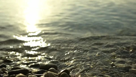 Scene of a lakeshore with pebbles in the lower foreground, reflection of the sun Stock Footage 248356519