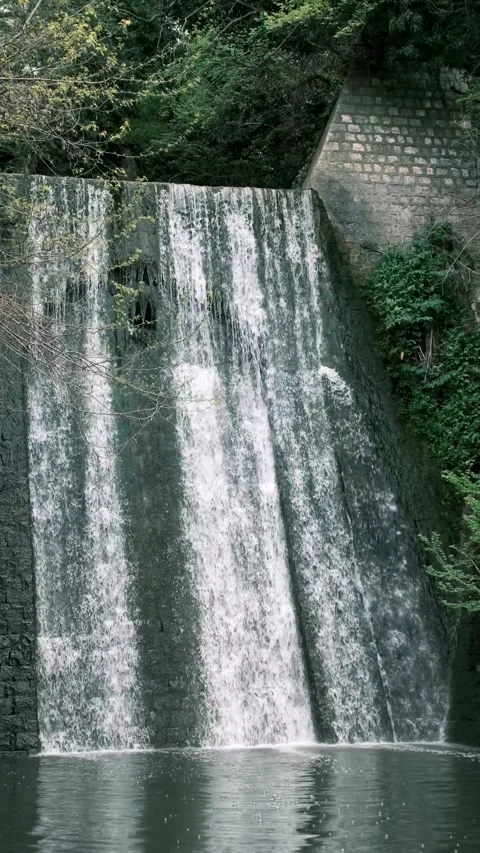 Scenic artificial stone waterfall cascading into a calm pond Vídeos de archivo 335045350