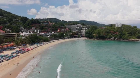 Scenic beach view with clear water, sunbathers, and lush hills in background Video stock 337419218