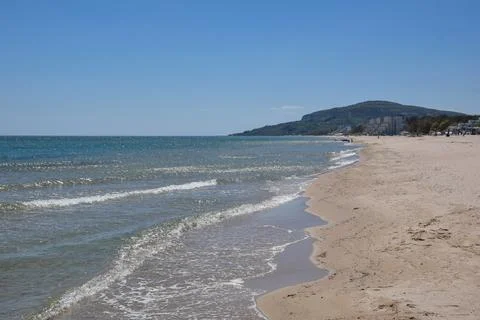 Scenic beach view with gentle waves and distant hills under clear sky Stock Photos