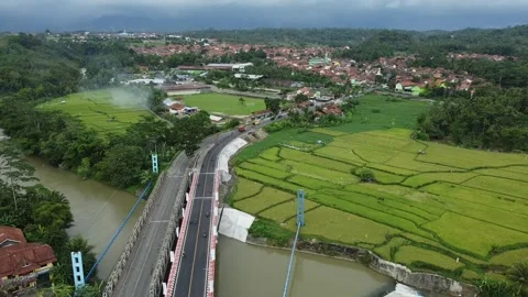 Scenic bridge crossing over a river with lush rice fields and village views Stock Footage 259554493