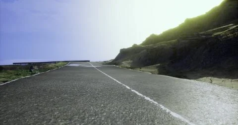 Scenic coastal road surrounded by cliffs and bright sky at sunset Stock Illustration