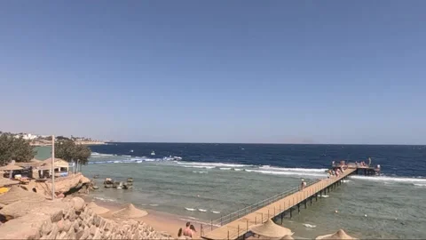 Scenic Coastal View Featuring a Pier, Sandy Beach, and Clear Blue Waters Under a Video stock 330099562