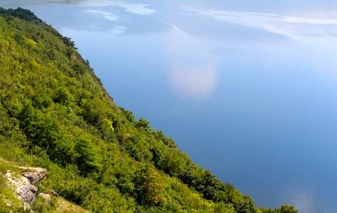Scenic high-angle view of a lush green forested slope meeting a vast blue w.. Stock Photos