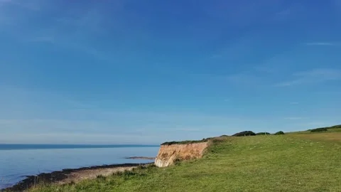 Scenic hilltop path overlooking ocean and coastal cliffs under clear summer sky Stock Footage 309768543