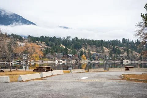 Scenic lakeside view with mountain backdrop, houses, and picnic benches. Stock Photos