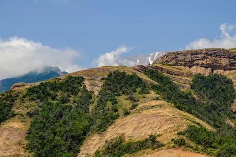 Scenic mountain range with greenery, dry earth, and snowy summits under blu.. Stock Photos