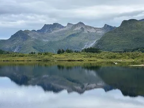 Scenic mountain range reflected in calm lake under cloudy sky Stock Photos